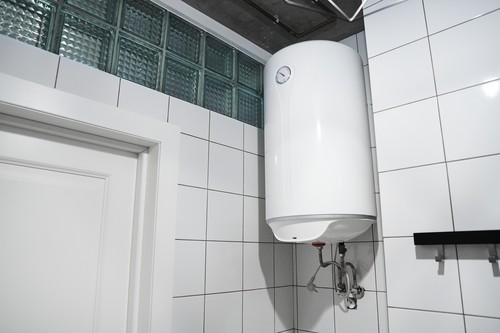 Modern Gas Tanked Boiler In Bathroom. Household Budget Water Heater Hanging On The Wall In Boiler Room. Сommon Electric Storage Tank Water Heater. Home Heating System In Front Of White Tiled Wall